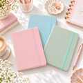 A5 pastel notebooks in pink, blue and sage green with matching elastic closures on a styled desk
